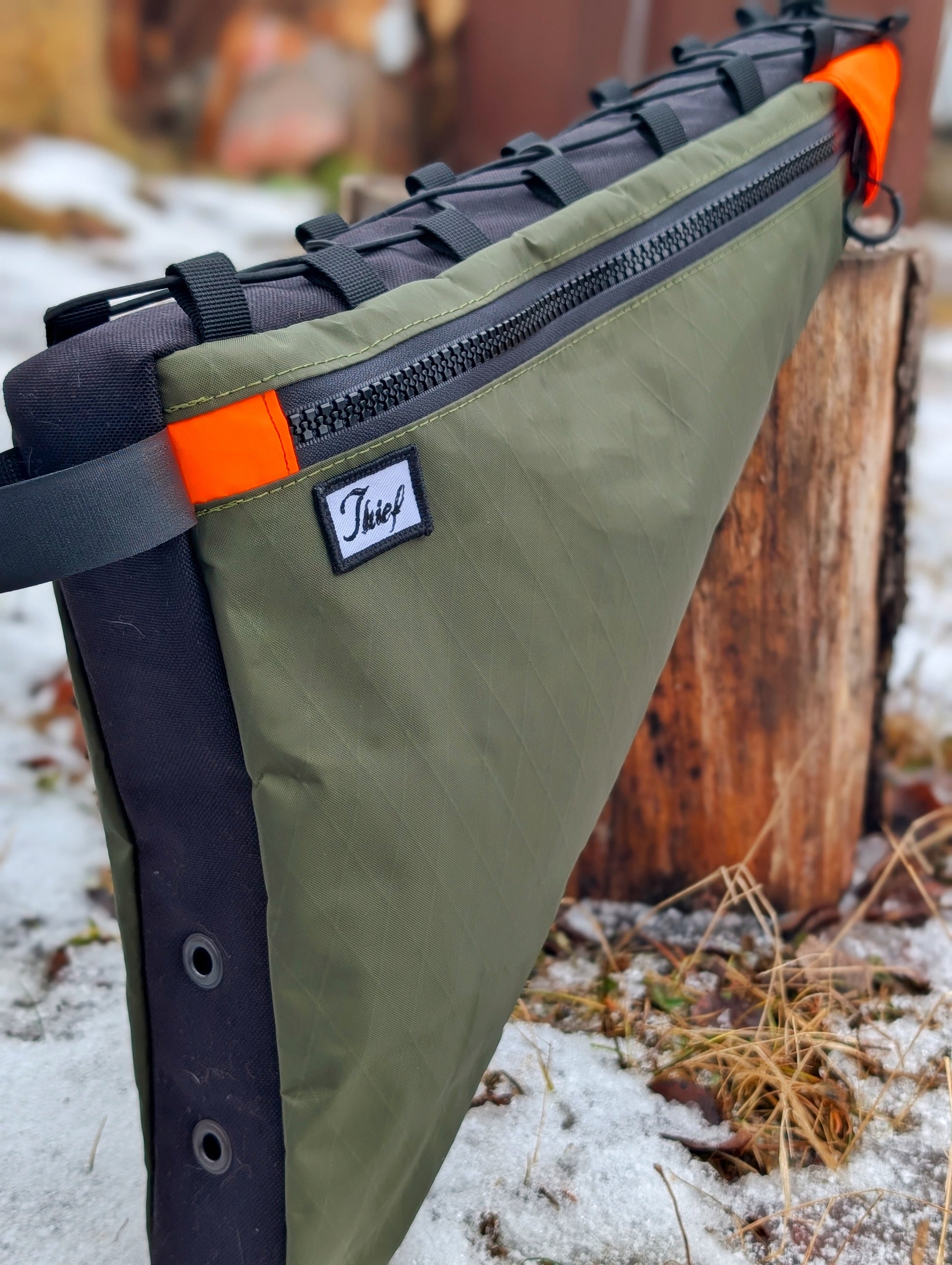 Green bag with black straps and orange accents on a snowy ground