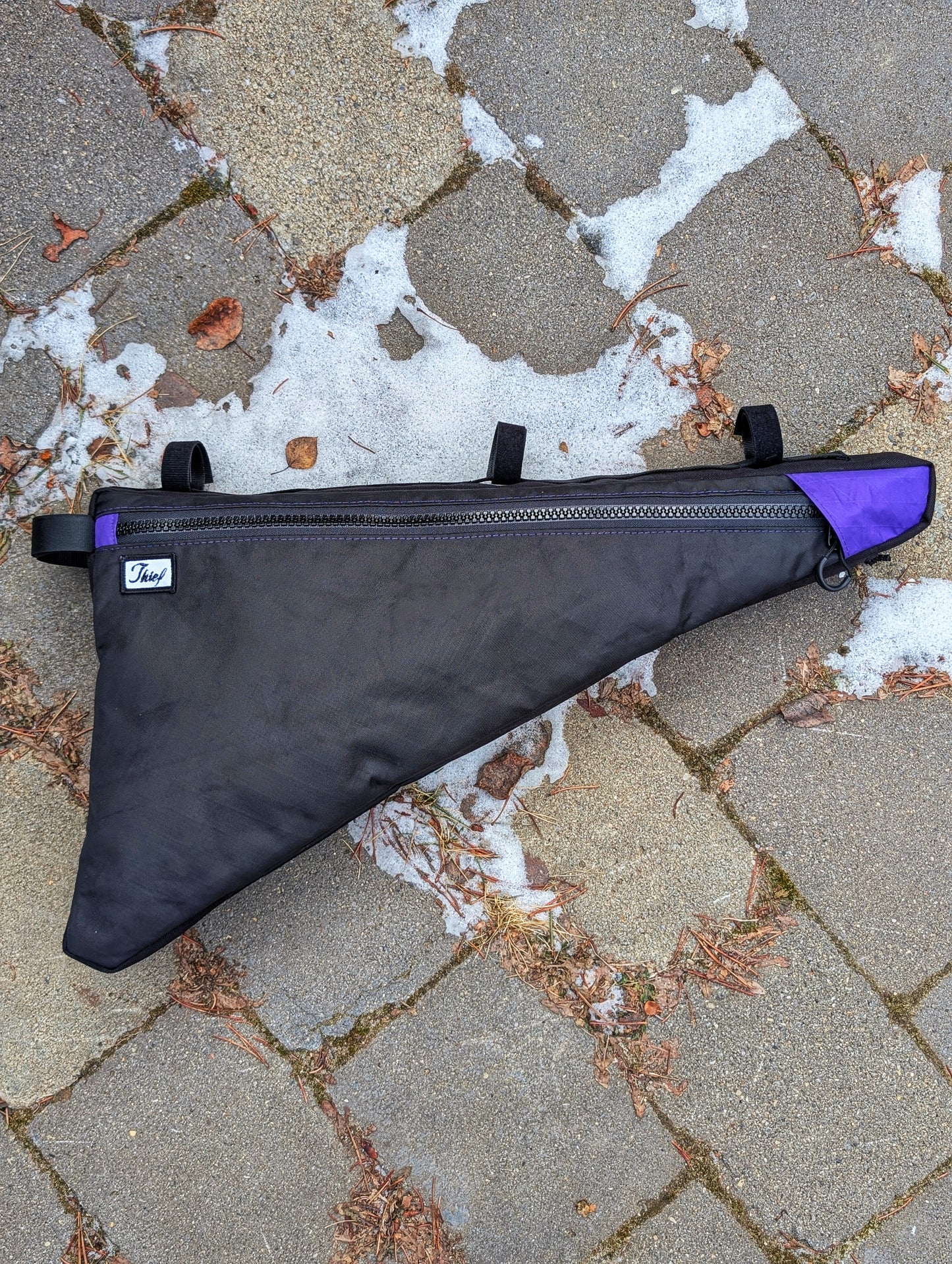 Black and purple bolt on frame bag on a stone pavement with snow patches
