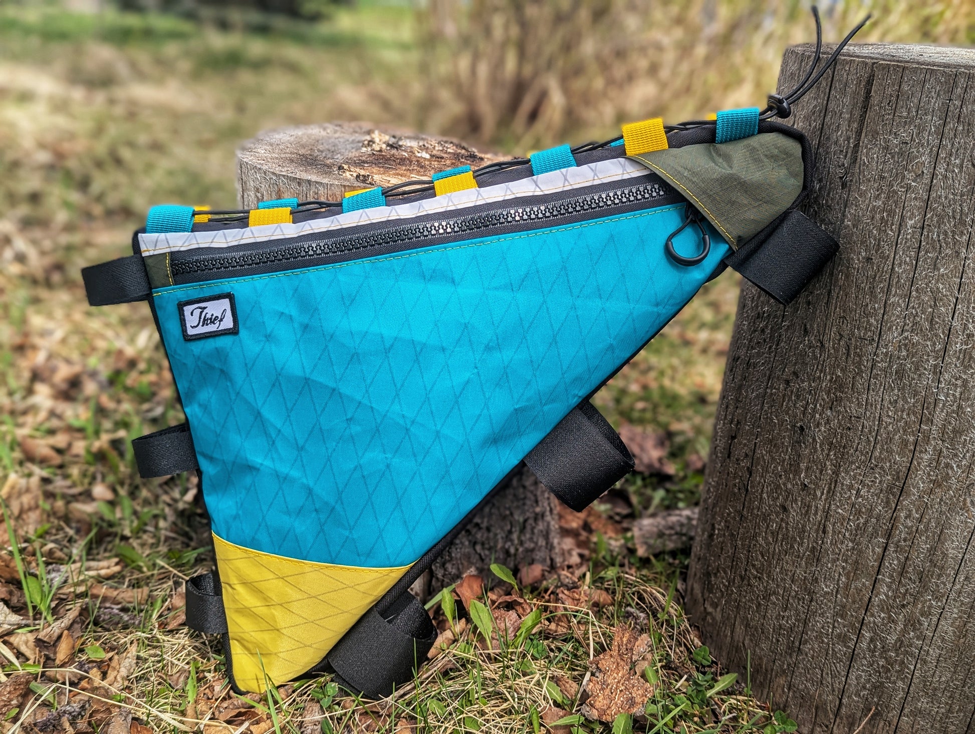 Blue and yellow bike frame bag attached to a wooden post outdoors