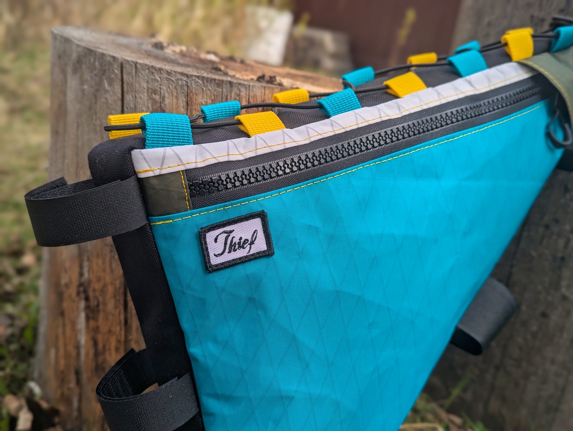 Teal bag with colorful straps attached to a wooden post outdoors