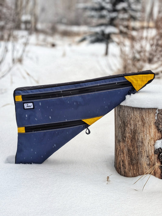 Blue and yellow double decker frame bag leaning against a wooden post in a snowy landscape