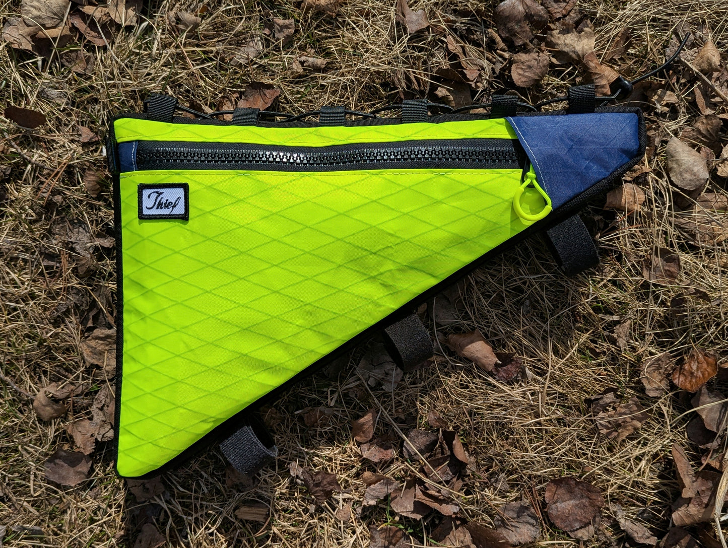 Triangular bag with green and blue sections on a ground covered with dry leaves